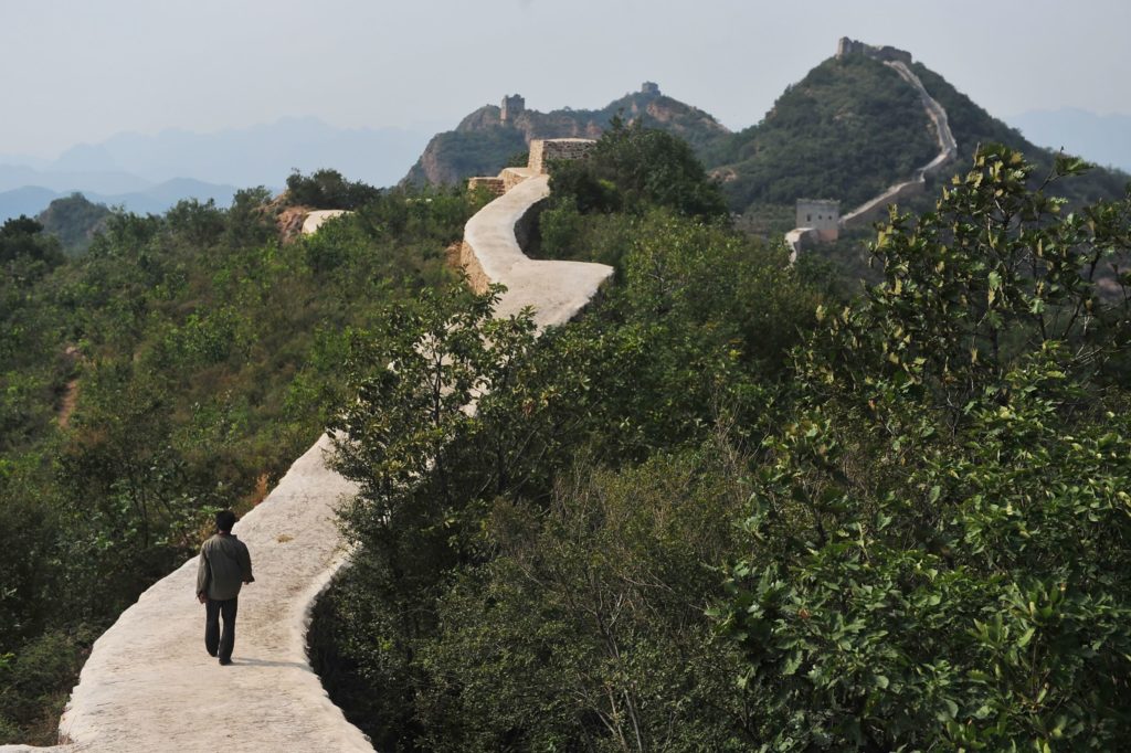 This picture taken on September 21, 2016 shows a villager walking on a paved-over section of the Great Wall of China at Suizhong, in China's northeast Liaoning province. Chinese social media users were in an uproar on September 23 over restoration of a 700-year-old section of the Great Wall that has been covered in concrete, turning it into a smooth, flat-topped path. Known as one of the most beautiful portions of the "wild", unrestored wall, the eight-kilometre (five-mile) Xiaohekou stretch in northeast Liaoning province was built in 1381 during the Ming Dynasty. / AFP PHOTO / STR / China OUT